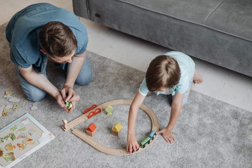 A therapist and a child playing with a wooden train set on a grey carpet